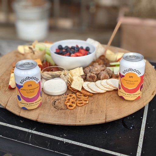 An outdoor photo of a charcuterie board with Soulboost cans